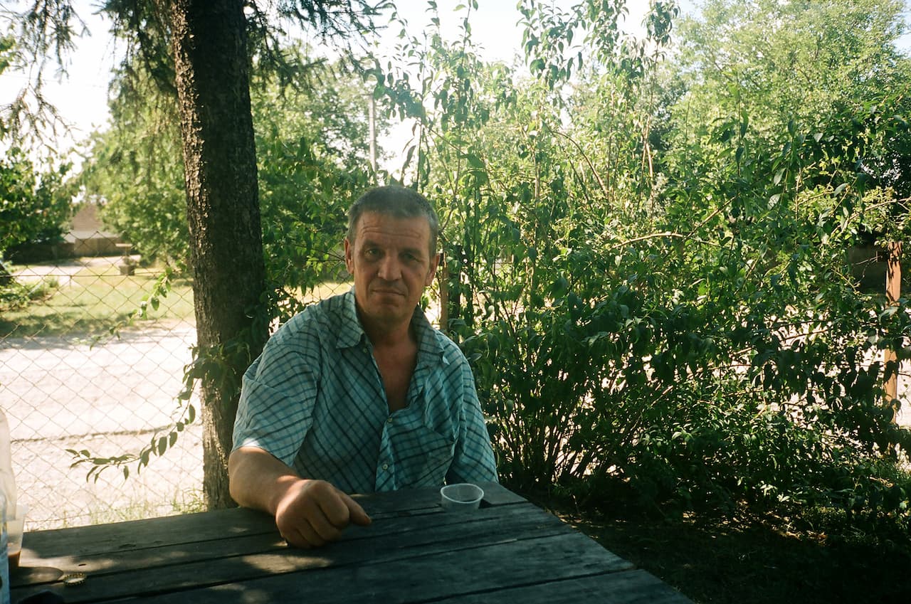 Чоловік сидить на лавці перед деревом